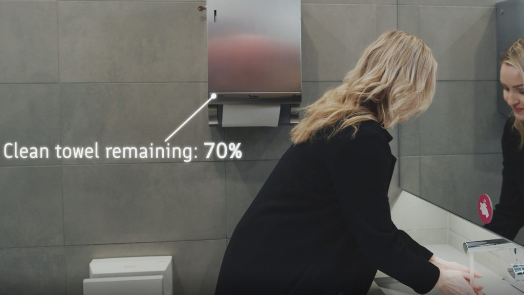 Woman washing hands with the hand towel dispenser displaying the amount of clean towel remaining. 