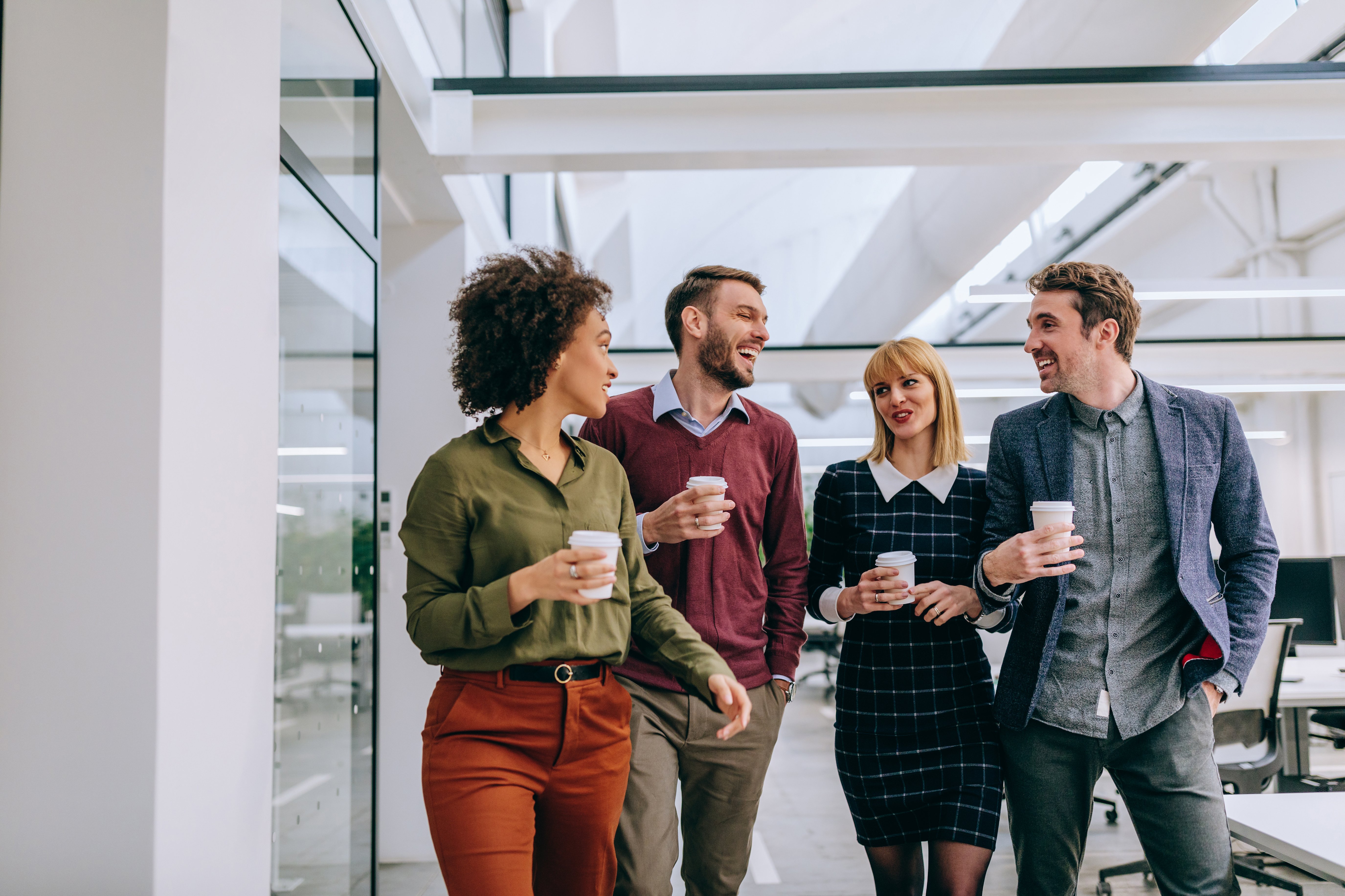 Group of diverse coworkers walking through a corridor in an office, holding paper cups