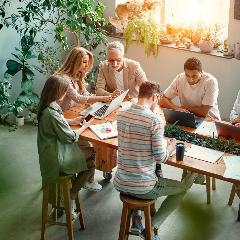 Multiracial creative people in modern office. Group of young business people and senior boss are working together with laptop, tablet, smart phone, notebook, graphs. Successful team in coworking