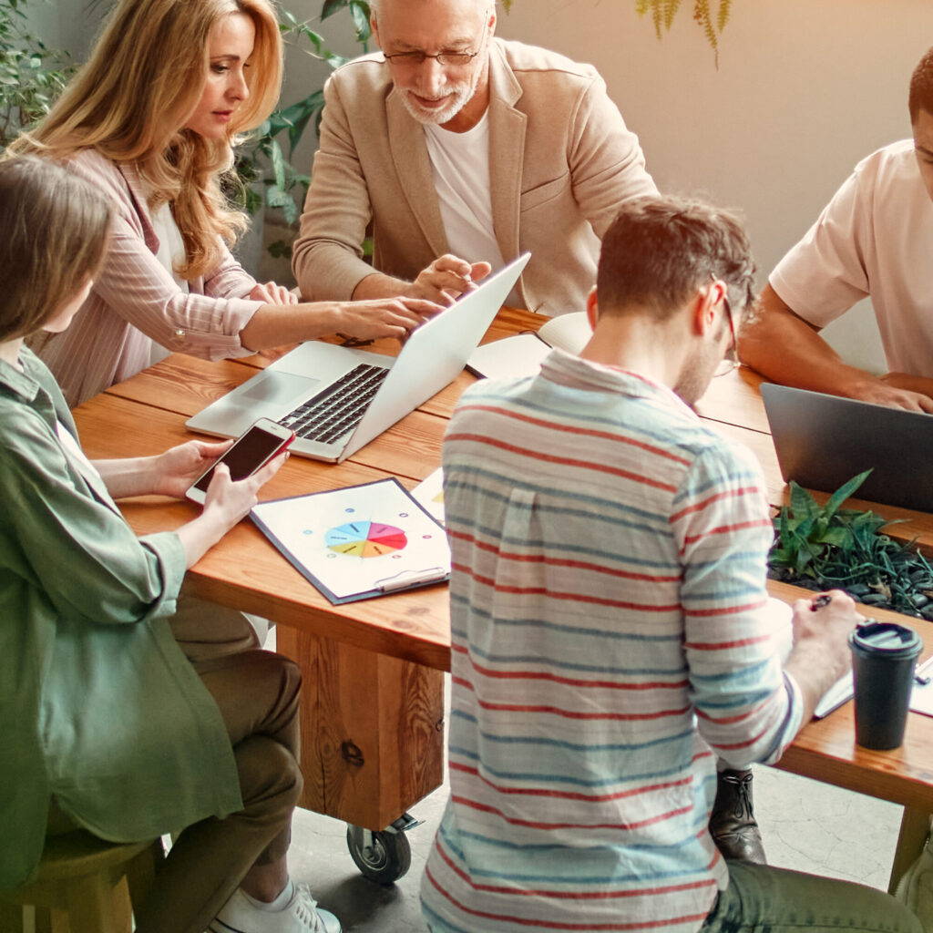 Multiracial creative people in modern office. Group of young business people and senior boss are working together with laptop, tablet, smart phone, notebook, graphs. Successful team in coworking