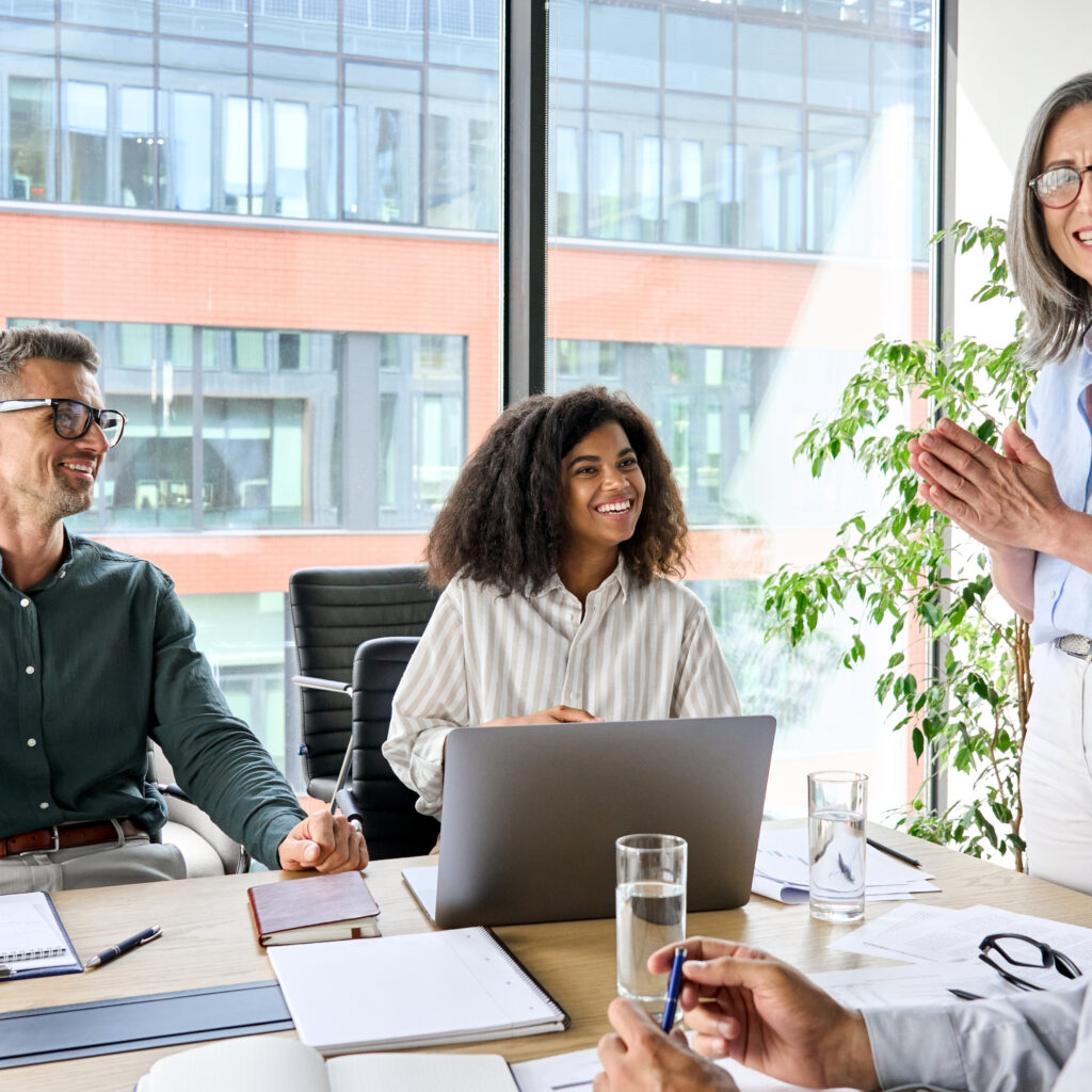 Senior older female executive ceo and happy multicultural business people discuss corporate project at boardroom table. Smiling diverse corporate team working together in modern meeting room office.